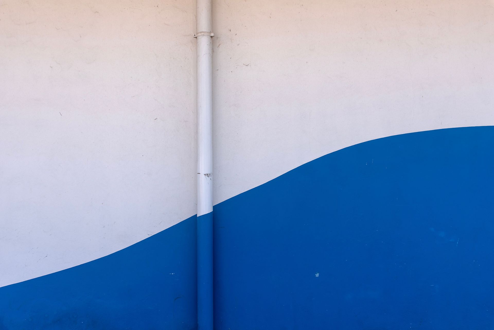 A minimalist abstract wall with a blue wave design and a vertical pipe.